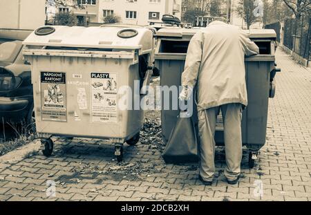 Ein Obdachloser nimmt einen Mülleimer heraus, während er eine Tasche in der Hand hält. Stockfoto