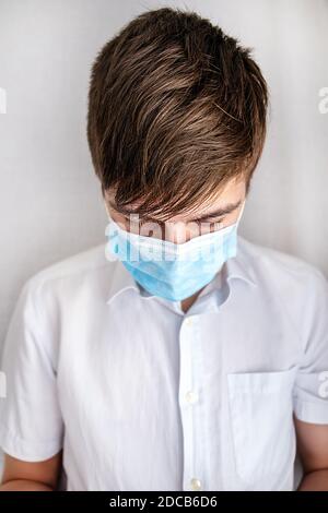 Trauriger und müder junger Mann in einer Grippe Maske von Die Wand im Raum Stockfoto