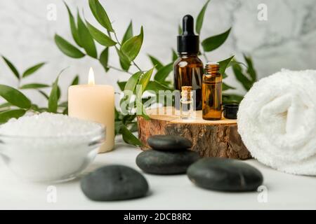 Schönheitsbehandlungen für Spa-Behandlungen auf weißem Holztisch mit grüner Pflanze. Massagesteine, ätherische Öle und Meersalz mit brennender Kerze Stockfoto