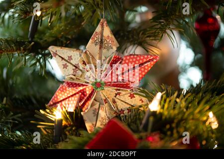 Geschmückter Weihnachtsbaum, echte Nordmann-Tanne vor verschwommenem Hintergrund. Makrofotografie zeigt einen 6-spitzen Stern aus Papier gefaltet. Stockfoto