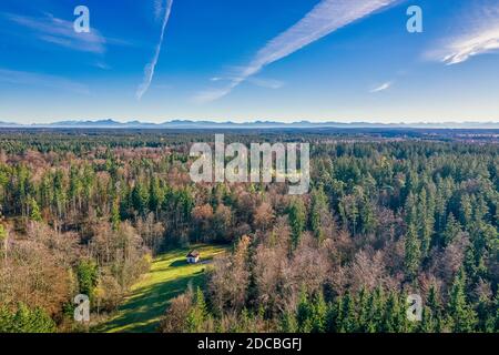 Luftbild auf einem Haus in einem idyllischen Grundstück mitten im Wald zur Herbstzeit mit den Alp-Bergen im weiten Hintergrund. Stockfoto