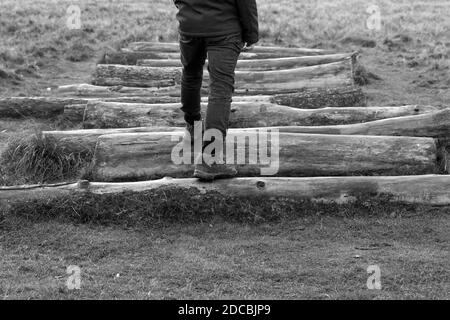 Schwarz-weiß-Bild mans Beine und Füße treten auf Holzbaum Stamm Protokolle außerhalb tragen Wanderschuhe.Männlich zu Fuß außerhalb Training im Winter Stockfoto