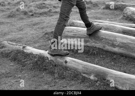 Schwarz-weiß-Bild mans Beine und Füße treten auf Holzbaum Stamm Protokolle außerhalb tragen Wanderschuhe.Männlich zu Fuß außerhalb Training im Winter Stockfoto