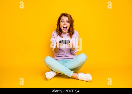 In voller Länge Foto von verrückten überrascht Frau sitzen bodenbeine Gekreuzt spielen Video Spiel gewinnen Wettbewerb schreien wow omg tragen tealrosa Pullover Kleidung isoliert Stockfoto