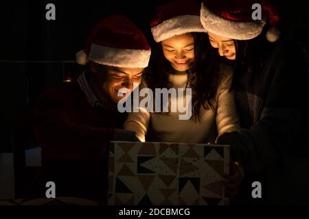 Fröhliches Familienportrait, Vater Mutter und Tochter, feiern Weihnachten und Neujahr zusammen, öffnen Geschenkbox mit magischer Überraschung Stockfoto