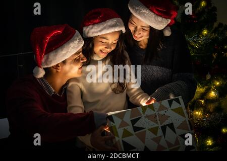 Fröhliches Familienportrait, Vater Mutter und Tochter, feiern Weihnachten und Neujahr zusammen, öffnen Geschenkbox mit magischer Überraschung Stockfoto