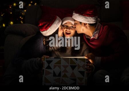 Fröhliches Familienportrait, Vater Mutter und Tochter, feiern Weihnachten und Neujahr zusammen, öffnen Geschenkbox mit magischer Überraschung Stockfoto