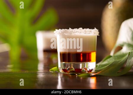 Tropische alkoholische Aufnahmen mit Kokosflocken, Monstera Blume mit Kokosnuss und Ananas auf braunem Holzhintergrund dekoriert Stockfoto