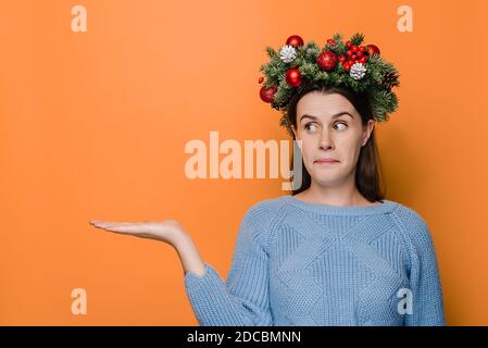 Junge Frau hat überrascht ahnungslosen Ausdruck, sieht angehoben Palme in Überraschung, Gesichter schwierige Situation, trägt handgefertigten Kranz und kuscheligen Pullover Stockfoto