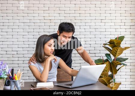 Asian Mann Mann motivieren Beratung Frau freiberuflich arbeiten zu Hause, sitzen am Schreibtisch Esstisch im Wohnzimmer Stockfoto