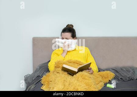 Frau liest Buch im Bett, mit Papierserviette niesen, erlebt Allergiesymptome, erwischt eine Erkältung, bleiben Isolation für Selbstquarantäne. Konzept zu Hause Stockfoto