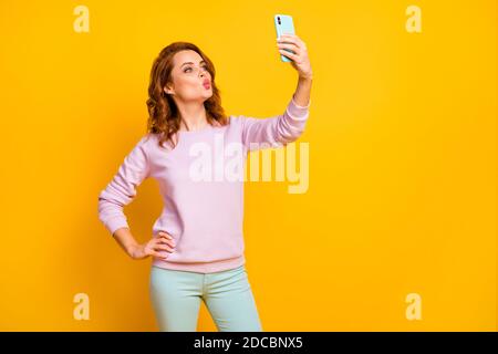 Foto von liebenswert hübsche Dame halten Telefon Hand machen Selfies Freund flirty Stimmung senden Luft Küsse tragen rosa Pullover grün Hose isoliert Stockfoto