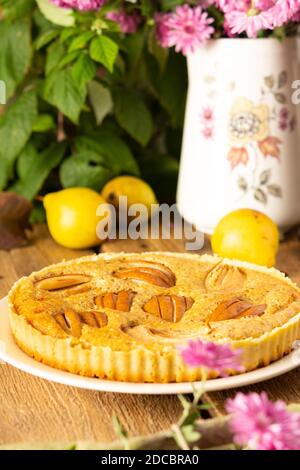 Köstlicher Birnenkuchen aus gelben Birnen auf Holzgrund, Himbeerbusch im Hintergrund, rosa Chrysanthemen in Vase, rustikaler Stil Stockfoto