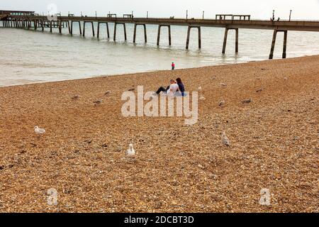 Ein Paar sitzt am Strand und picknickt neben Deal Pier während covid Einschränkungen, sie sind von Möwen umgeben in der Hoffnung, Essen zu bekommen, Deal, Kent, Großbritannien Stockfoto