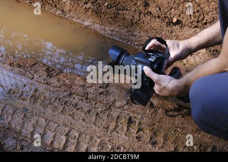 Eine DSLR-Fotomaschine in den Händen des Fotografen in der Natur. Er versucht, ein Spiegelbild auf einem schlammigen Wasser zu machen. Stockfoto