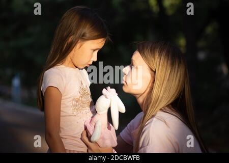 Junge Mutter umarmt ihre weinende kleine Tochter. Traurige Tochter in den Armen ihrer Mutter. Stockfoto