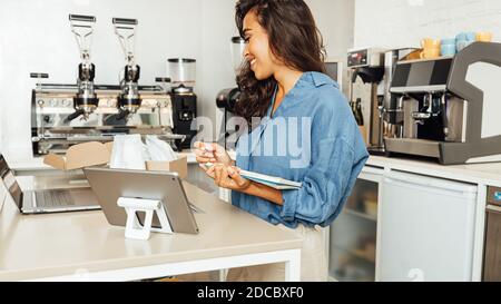 Seitenansicht einer Geschäftsfrau in Casuals, die in ihrem Café steht und eine Warenbuchhaltung anstellt. Stockfoto