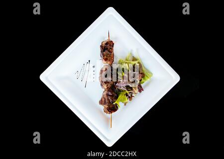 Schweinekebab auf einem Stock auf einem Teller mit Grün Salat Stockfoto