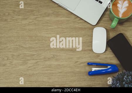 Smartphone, Maus und Kaffeetasse auf dem Schreibtisch aus Holz mit Laptop-Computer und Zubehör. Draufsicht mit Kopierplatz, flach liegend. Stockfoto