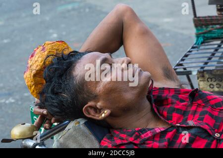 Alltag in Myanmar - Mann liegt mit geschlossenen Augen am Fahrrad und hält Tabakblatt in Yangon, Myanmar (Burma), Asien im Februar Stockfoto