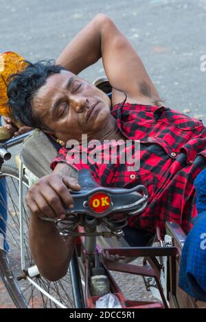 Alltag in Myanmar - Mann liegt mit geschlossenen Augen am Fahrrad und hält Tabakblatt in Yangon, Myanmar (Burma), Asien im Februar Stockfoto