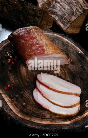 Frisch geräuchertes Stück Schweinehund, in Scheiben geschnitten, auf einem Holzhintergrund mit Eichenstumpf ausgelegt. Nahaufnahme Stockfoto