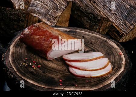 Frisch geräuchertes Stück Schweinehund, in Scheiben geschnitten, auf einem Holzhintergrund mit Eichenstumpf ausgelegt. Nahaufnahme Stockfoto