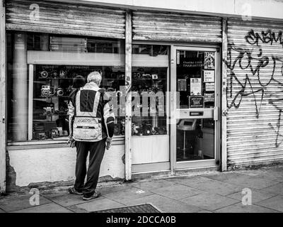 Man Schaufenster Shopping für Kameras in Camden Town London mit teilweise geschlossenen Stahlfenstern mit Graffiti auf ihnen in einem Schwarz-Weiß-Ton, 15 Aug 2020 Stockfoto