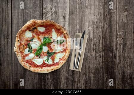 Blick von oben auf Pizza auf Holztisch mit Besteck Stockfoto