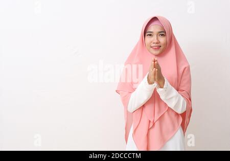 Eine asiatische Frau in muslimischer Kleidung steht in einer Grußpose Namaste Händen, begrüßt Gäste, IED Fitr Gruß. Isoliert auf weißem Hintergrund Stockfoto