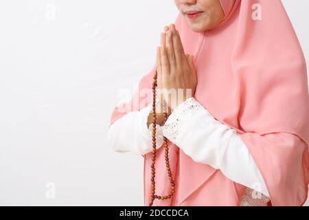 Eine asiatische Frau in muslimischer Kleidung steht in einer grüßenden Pose zu Namaste Händen, begrüßt Gäste, IED Fitr Gruß, während eine Gebetskette hält. Isola Stockfoto