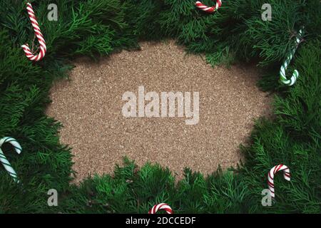 Rahmen aus Nadelholzzweigen und Zuckerstöcken auf einem Korkbrett. Weihnachten Stockfoto