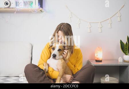 Junge Frau umarmt ihren Hund, Innenschlafzimmer Szene. Freude von Haustieren zu Hause oder während Aussperrung oder Selbstisolation, kalte Wintersaison Stockfoto