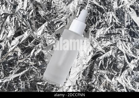 Serum mit Kollagen und Peptiden auf zerknitterter Silbermetallfolie. Hyaluronsäure-Öl-Tinktur auf faltiger Aluminiumtinktur. Beauty-Produkt Stockfoto