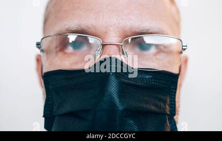 Porträt eines Mannes in einer verdunkelten Brille und einer schwarzen Gesichtsmaske während einer COVID-19-Weltpandemie beim Blick auf die Kamera. Virus Selbstschutz und Vision Gesundheit Co Stockfoto
