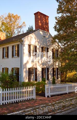 Weißer Pfostenzaun und ein Haus an einer Straße in Dicheyville, der Kolonialzeit, historische Mühlenstadt. Im Herbst in Baltimore, Maryland. Stockfoto