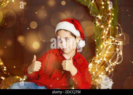 Lustiger Junge in den Winterabenden vor dem Hintergrund der Weihnachtsbeleuchtung Stockfoto