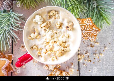 Popcorn Latte Kaffeebecher. Trendiges Heißgetränk, Latte mit gesalzenem Käse-Popcorn, mit winterlicher Weihnachtsdekoration, weißer Holzhintergrund-Kopierraum Stockfoto