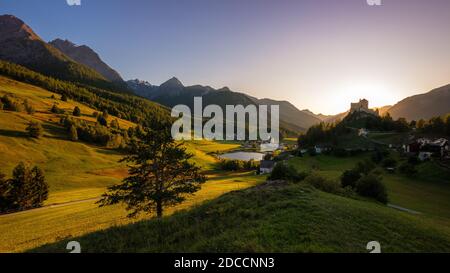 Die Sonne geht in den Bergen um Tarasp und seine Burg im Kanton Graubünden (Engadin) in der Schweiz unter. Stockfoto