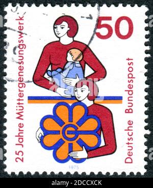 Eine in Deutschland gedruckte Briefmarke, die dem 25-jährigen Jubiläum der Stiftung für Wiedergeburtmutter gewidmet ist, zeigt Mutter mit Kind und Emblem, um 1975 Stockfoto