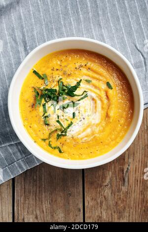 Kürbis-Karotten-Cremesuppe in einer weißen Schüssel auf einem Holztisch, Draufsicht. Stockfoto