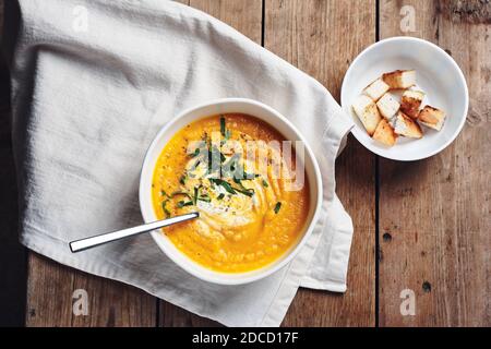 Kürbis-Karotten-Cremesuppe in einer weißen Schüssel auf einem Holztisch, Draufsicht. Stockfoto