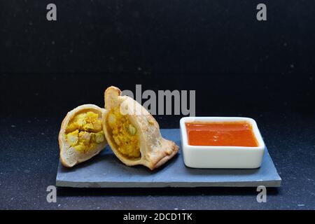 Moderne Samosa serviert mit roten heißen Sauce auf einem grauen Brett und ein dunkler Marmorhintergrund Stockfoto