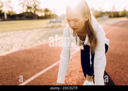 Athletic Girl in Sportswear, an der Startlinie im Rennen. Eine Läuferin startete den Sprint von der Startlinie aus vor dem Hintergrund der daw Stockfoto