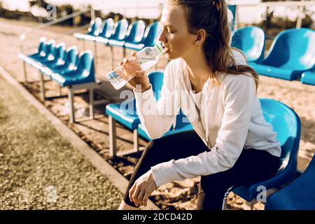 Müde Sportlerin trinkt Wasser aus der Flasche entspannt sich nach dem Training, eine Frau ruht nach dem Fitnessunterricht im Morgengrauen Stockfoto