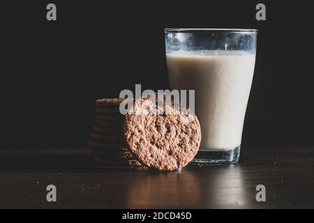 Serviert gesundes Frühstück mit einer frischen Milch in einem Glas und Stapel von köstlichen Schokolade hausgemachte Chip Cookies auf einem vintage dunklen Hintergrund. Foo Stockfoto