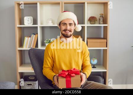 Junge positive Mann in Weihnachten Satna Hut sitzend Urlaub In Händen Stockfoto