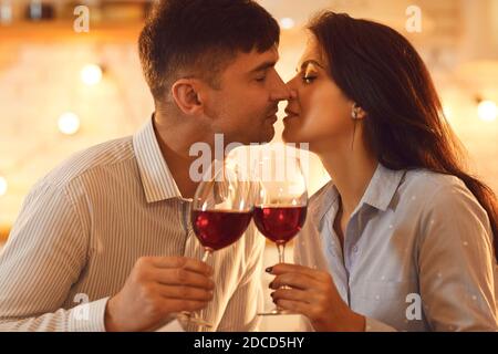 Junge liebevolle Paar küssen sich gegenseitig und hält Gläser von Wein während der Valentinstagsfeier Stockfoto