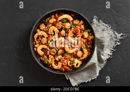 Kreolischer Stil Jambalaya mit Huhn, geräucherten Würstchen und Gemüse in Bratpfanne auf schwarzem Stein Hintergrund. Draufsicht, flach liegend, Nahaufnahme Stockfoto