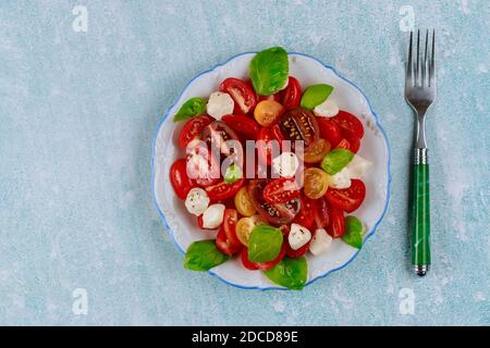 Kirschtomate mit Mozzarella-Käse auf weißem Teller mit Gabel. Nahaufnahme. Stockfoto